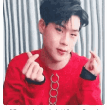 a young man is wearing a red sweater and making a heart shape with his hands .