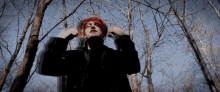 a woman with red hair and a black jacket stands in the woods