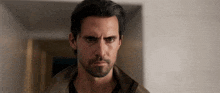 a man with a beard and a brown jacket looks at the camera