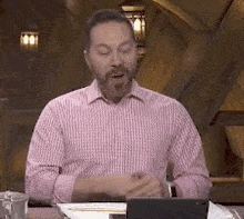 a man in a pink shirt is sitting at a table with his eyes closed and a laptop .