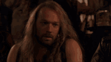a man with long hair and a beard is smoking a cigarette .