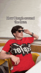a man wearing sunglasses and a red shirt with the words how i laugh around the huzz written on it