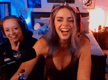 two women wearing headphones are laughing in front of a shure microphone in a bedroom .
