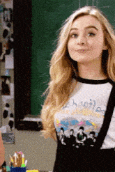 a girl wearing a beatles shirt is standing in front of a chalkboard .