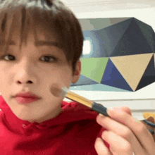 a close up of a person applying makeup with a brush in front of a geometric painting
