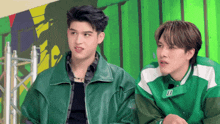 two young men are standing next to each other and one of them is wearing a green jacket with the letter b on it