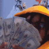 a person in a yellow hoodie is holding a stack of money in front of their face
