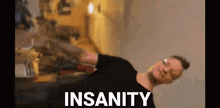 a man in a black shirt is dancing in a room with the word insanity written on the screen .