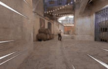a man walking down a street with barrels stacked on the side