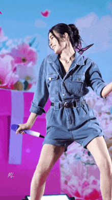 a woman in a denim jumpsuit is holding a microphone in front of flowers