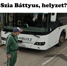 a man in green stands in front of a white bus that says nbusz on the front