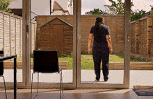 a woman stands in front of a sliding glass door looking out to a backyard