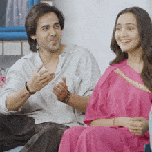a man and a woman are sitting on a couch and the woman is wearing a pink dress