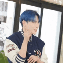 a man with blue hair is wearing a boston baseball jacket and earrings .