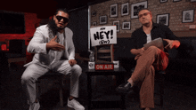 two men are sitting in front of a sign that says " hey "