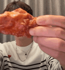 a man wearing a striped shirt is holding a piece of fried chicken in front of his face