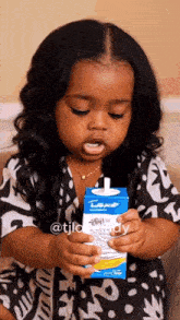 a little girl is sitting on a couch holding a carton of milk .