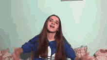 a young girl is sitting on a bed with her arms outstretched and wearing a blue adidas hoodie .