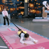 a man is pulling a person on a leash on a pink mat that says ad