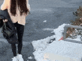 a woman in a white sweater and black leggings is walking on a snowy sidewalk .