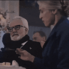 a man with glasses and a beard is smiling while a woman feeds him