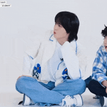 a man in a white jacket sits on the floor next to a man in a plaid shirt