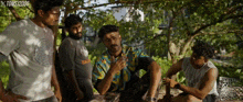 a group of men are gathered under a tree and one of them is wearing a shirt that says ' balm ' on it