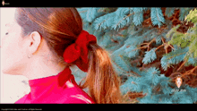 a woman wearing a red shirt and a red scrunchie stands in front of a blue tree