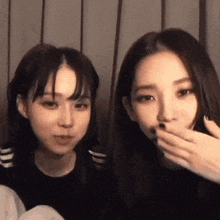 two girls are sitting next to each other and one is covering her mouth with her hand .