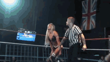 a woman in a wrestling ring with a referee and a british flag in the background