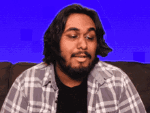 a man with a beard wearing a plaid shirt is sitting on a couch
