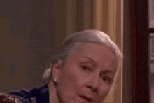 an elderly woman is sitting in front of a window and looking at the camera .