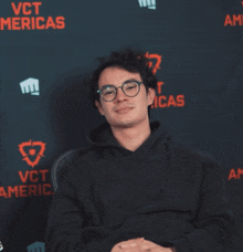 a man wearing glasses stands in front of a wall that says vct merica 's