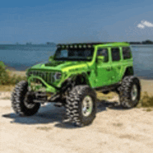 a green jeep is parked on a sandy beach next to the water .
