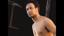 a man without a shirt is standing in front of a black background and looking at the camera .