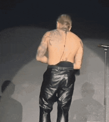 a shirtless man in leather pants stands in front of a microphone on a stage