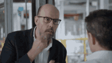 a man in a suit and glasses talks to another man