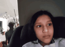 a girl sitting in a car seat looking at the camera with a chandelier in the background