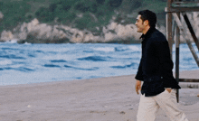 a man in a black jacket walks on a beach