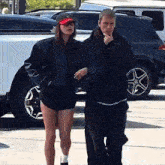 a man and a woman are walking down a street in front of a white suv
