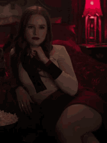 a woman in a red skirt sits on a couch with popcorn