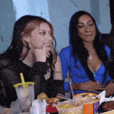 two women are sitting at a table with a cup that says survival on it