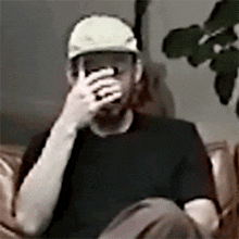 a man wearing a white hat is sitting on a couch covering his face with his hand