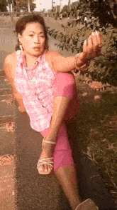 a woman in a pink plaid shirt and pink pants is sitting on a concrete wall giving the middle finger