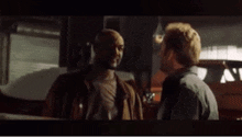 two men are standing next to each other in a dark room and talking .