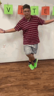 a man in a striped shirt and shorts is standing on one leg with his arms outstretched in front of a wall .