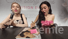 two women sitting at a table with a sign that says emle on it