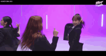 a group of women are dancing in front of a purple wall .