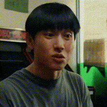 a young man in a gray shirt is sitting in front of a green wall .