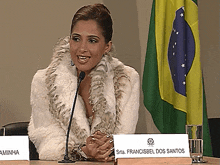 a woman in a fur coat sits at a table with a name plate that says srta francisbel dos santos